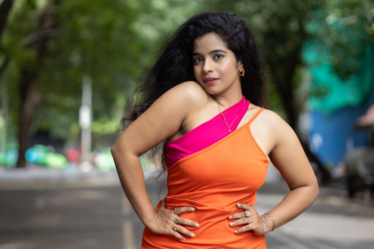 Vibrant portrait of a woman in an orange dress posing confidently outdoors.